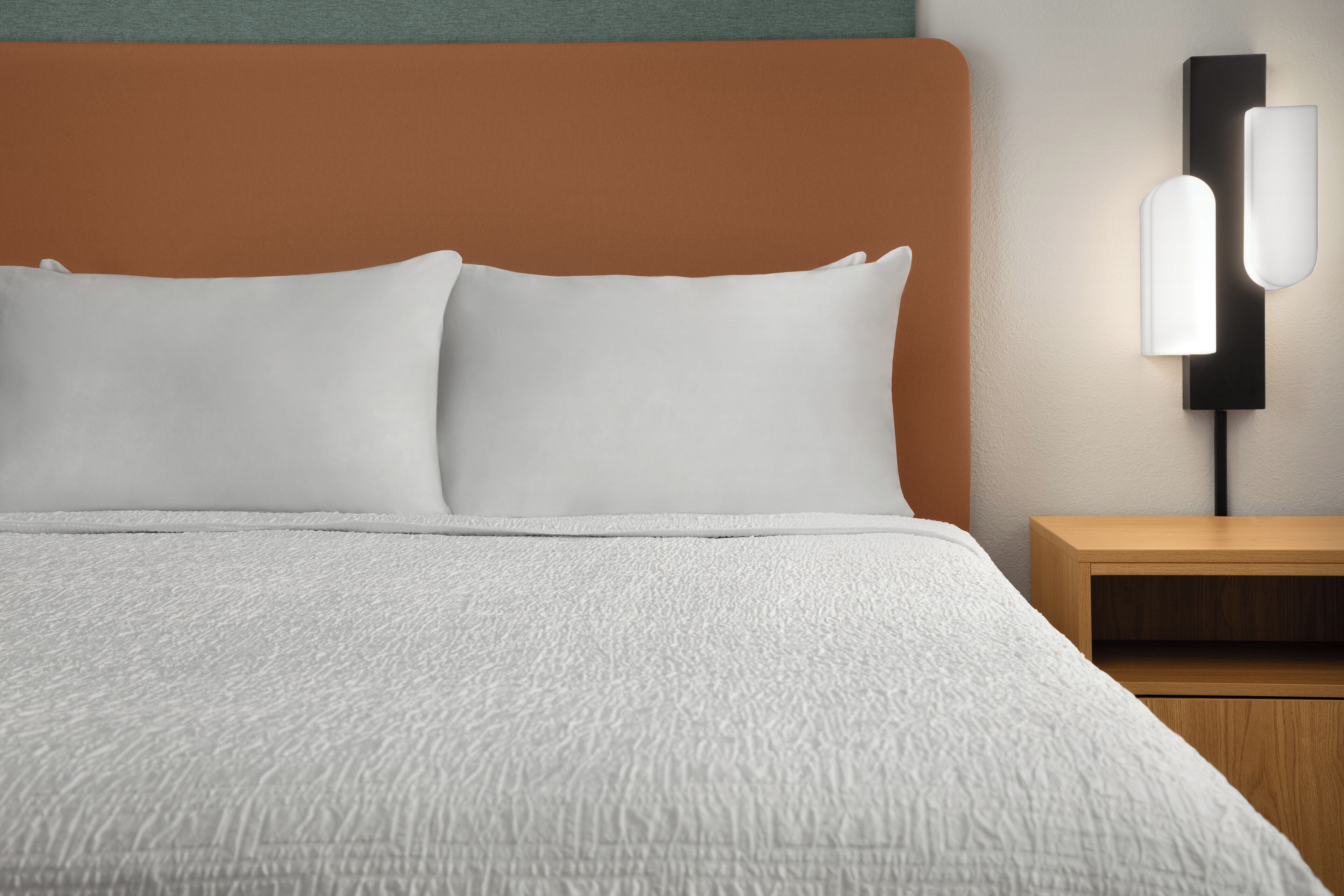 A neatly made bed with white bedding, a wooden headboard, and a bedside table with a lamp.