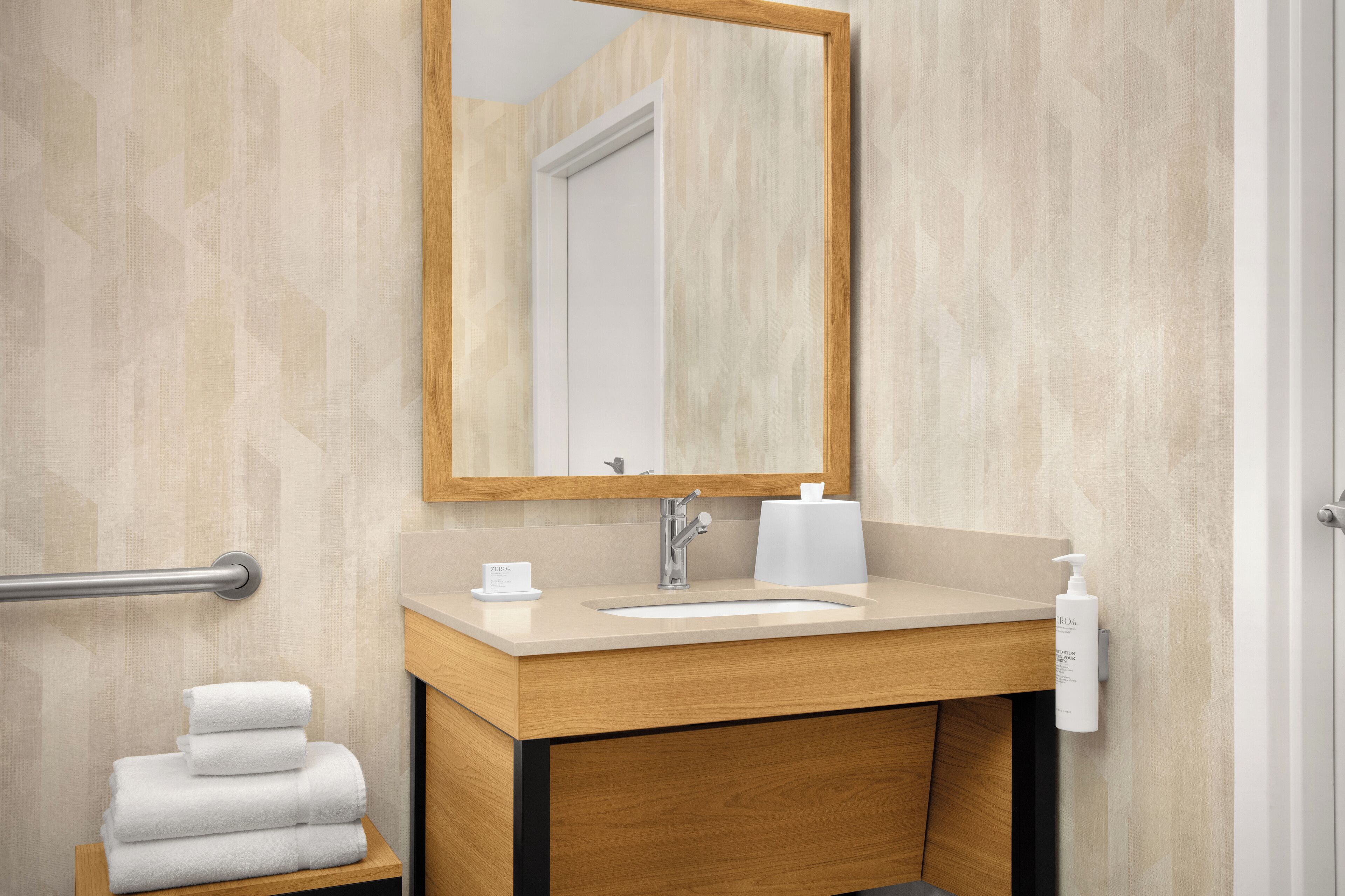 A bathroom with a wooden vanity, a sink, a mirror, a towel rack, and a bottle of hand soap.