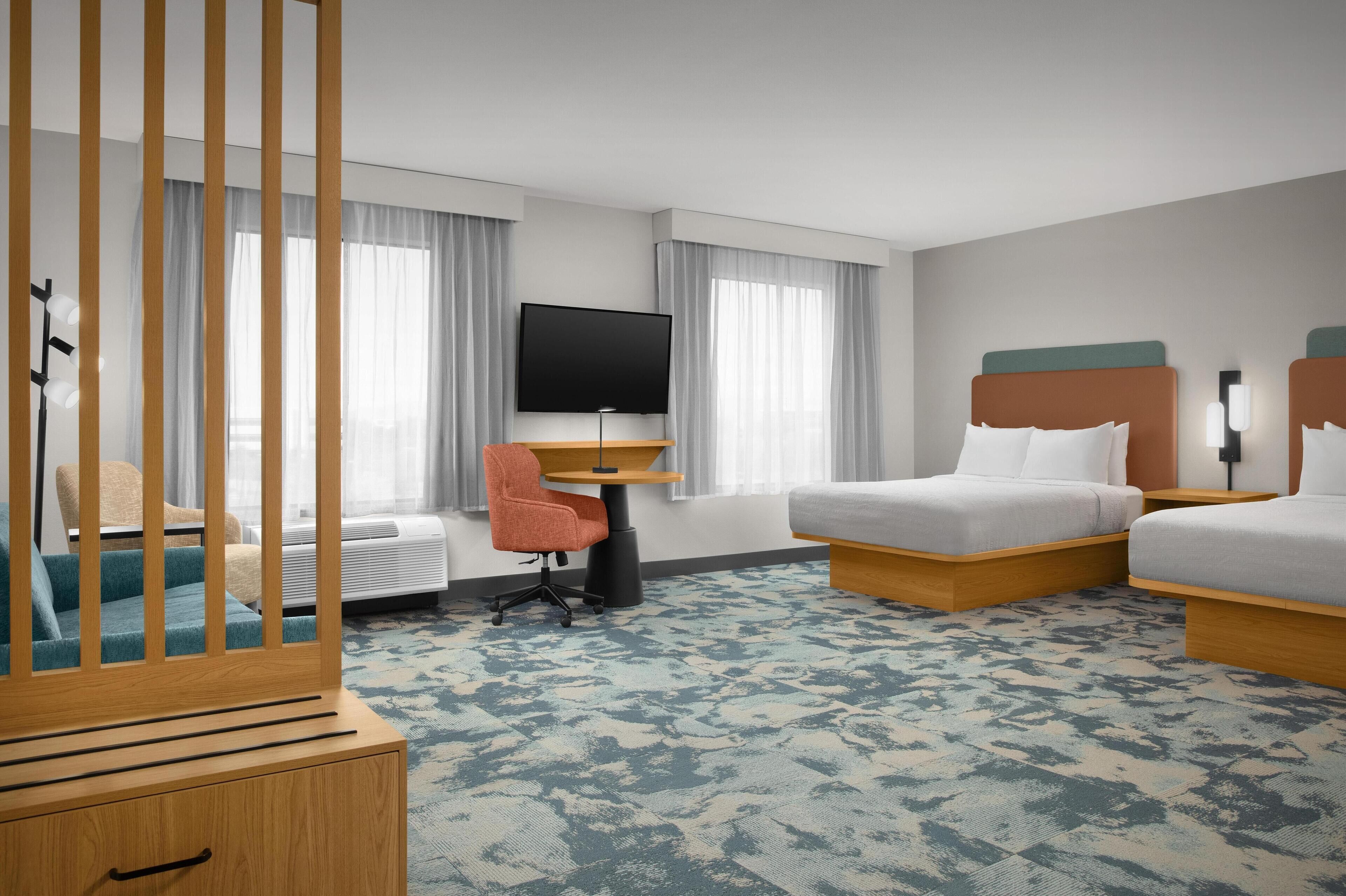 A hotel room with a bed, a desk with a TV, a chair, and a wardrobe.
