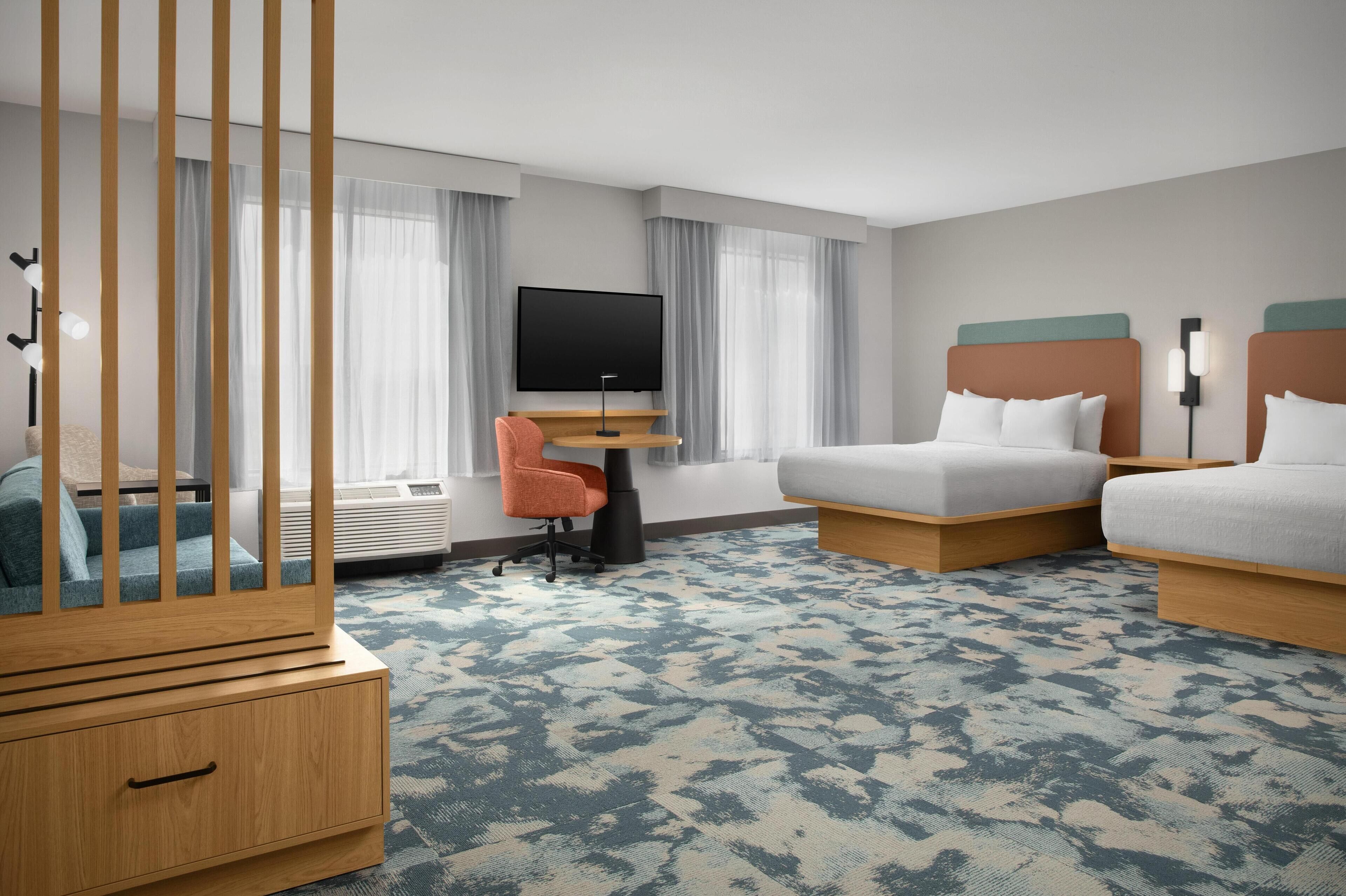 Ein Hotelzimmer mit Bett, Schreibtisch mit Fernseher, Stuhl, Kleiderschrank und einem großen Fenster mit Vorhängen.