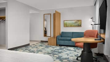 A hotel room with a bed, a sofa, a small table, a TV, and a painting on the wall.