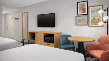 Una habitación de hotel con dos camas, un televisor, un armario de madera, una silla azul, una silla naranja y una mesa redonda.