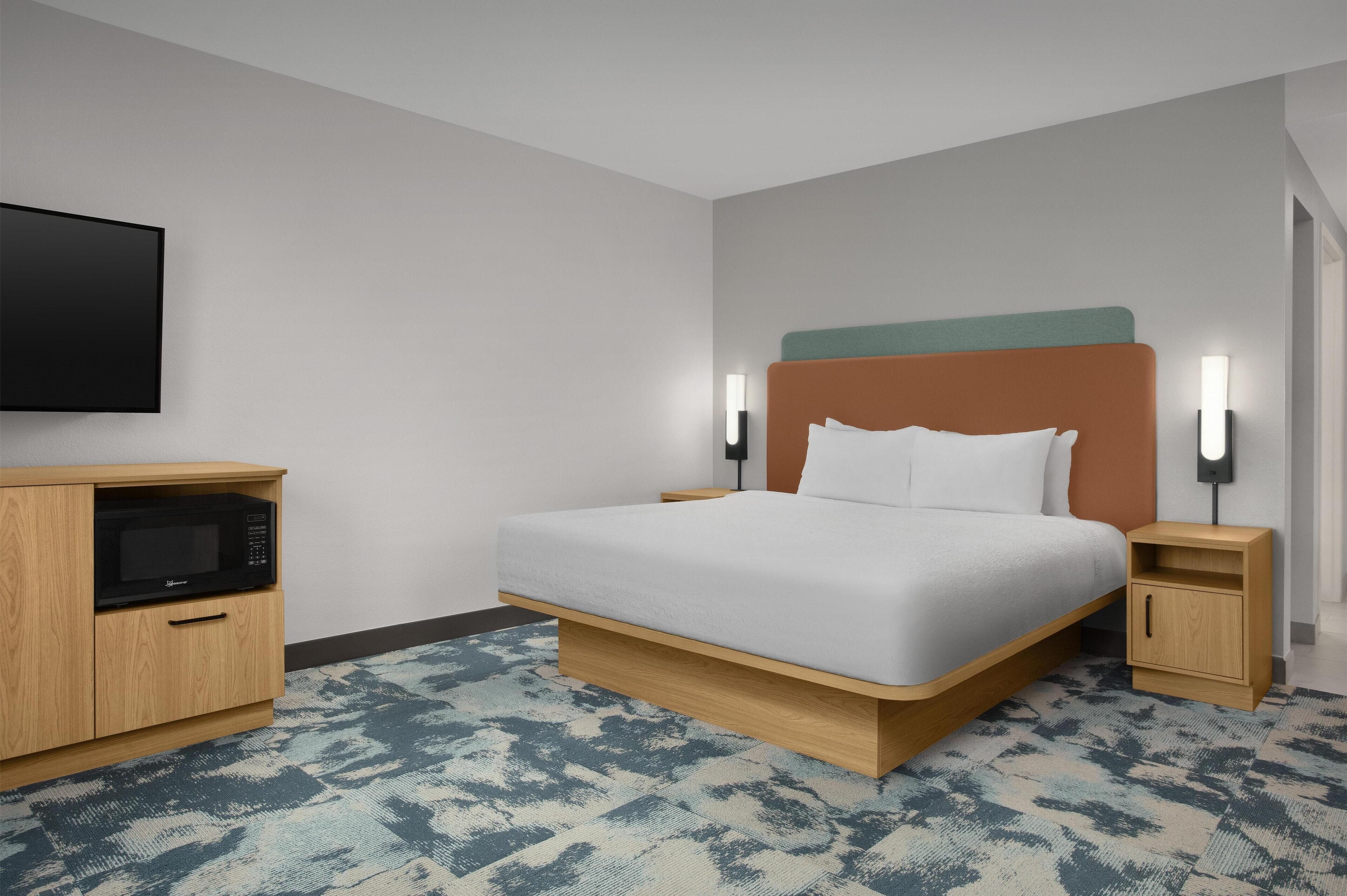 Una habitación de hotel con cama, televisión, microondas y mesita de noche.