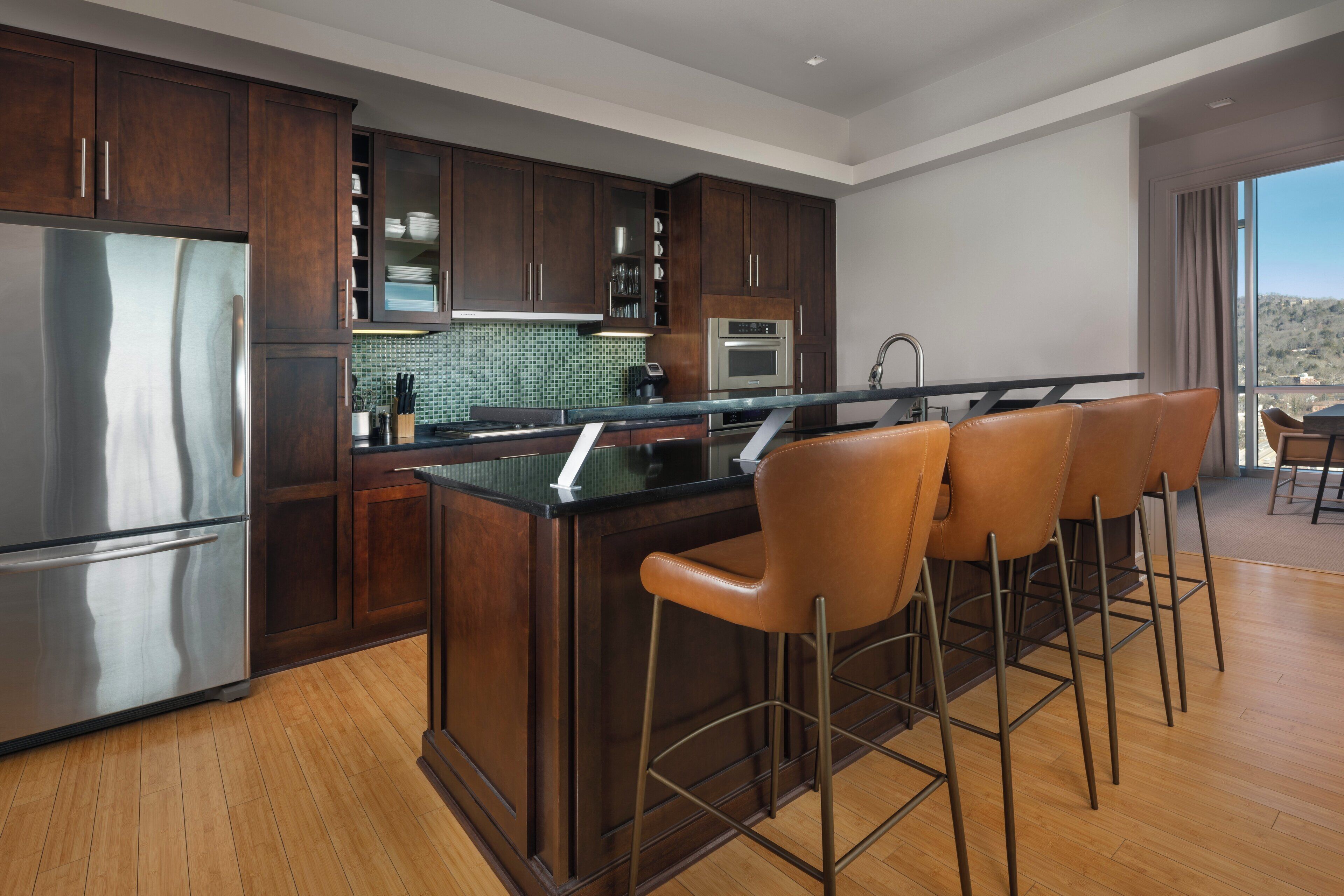 Una cocina moderna con armarios de madera oscura, un refrigerador de acero inoxidable, un horno empotrado y una zona de bar con taburetes de cuero.
