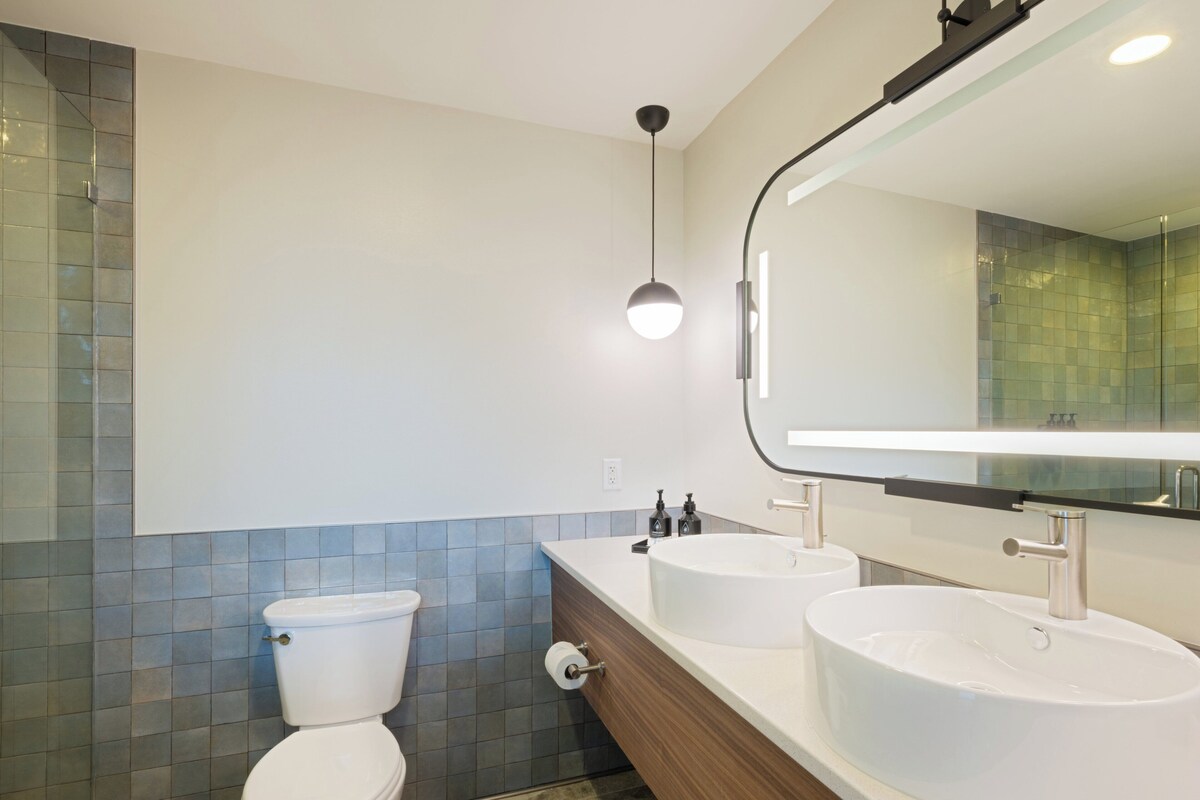 A modern bathroom with a toilet, two sinks, and a mirror.