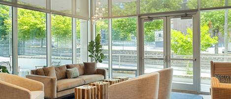 Un hall espacioso con ventanas amplias, un sofá, sillones y mesas de centro de madera.