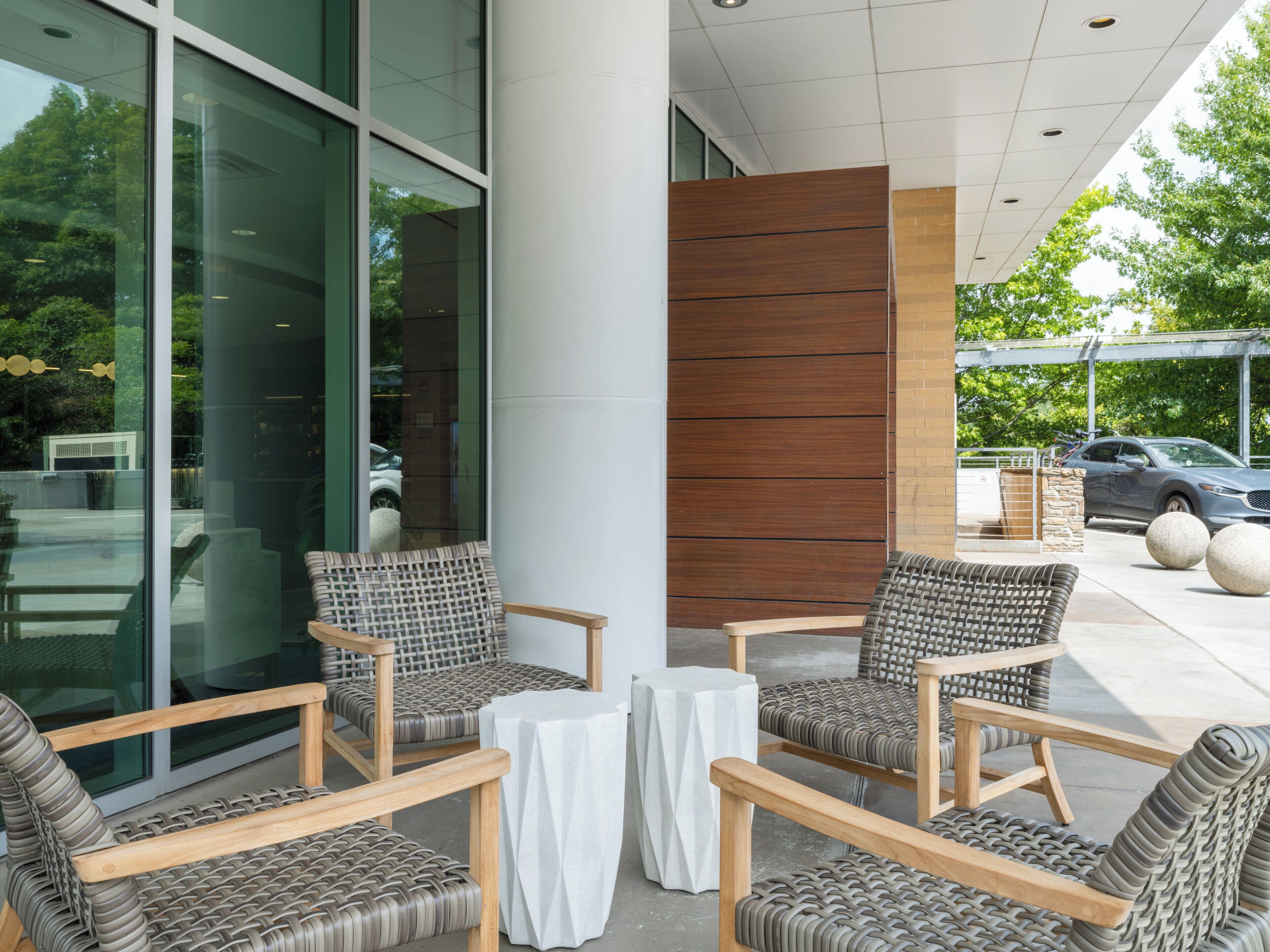 A modern outdoor seating area with wicker chairs and tables, large windows, and a view of the street.