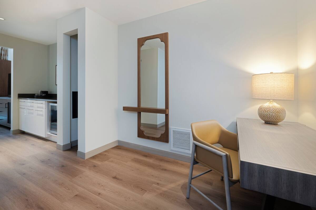 A modern room with a wooden floor, a desk with a lamp, a chair, and a large mirror on the wall.