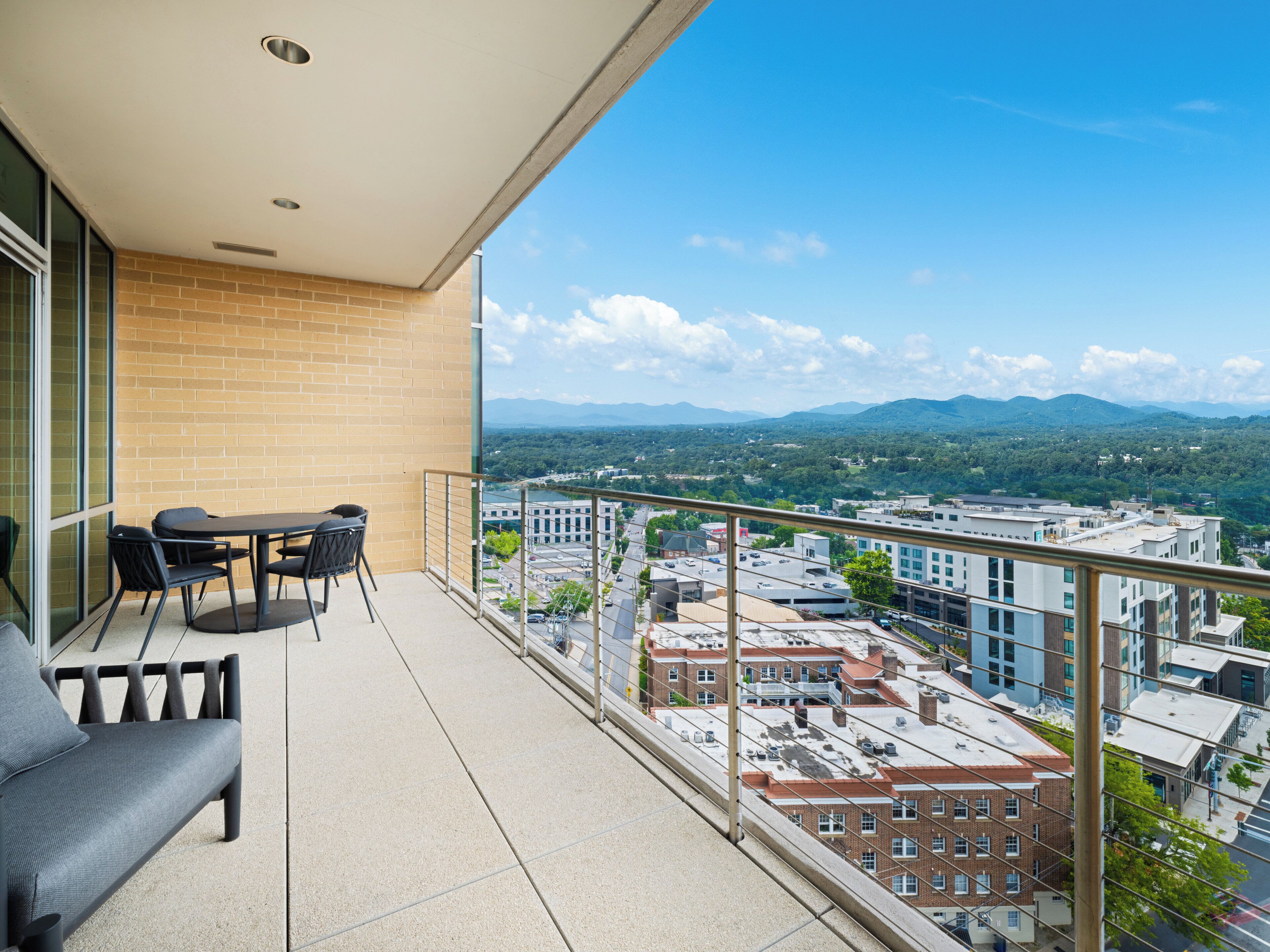 A balcony with a sofa and chairs, offering a view of a cityscape and mountains.