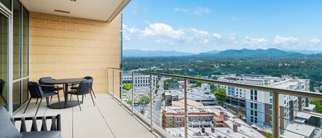 A balcony with a sofa and chairs, offering a view of a cityscape and mountains.