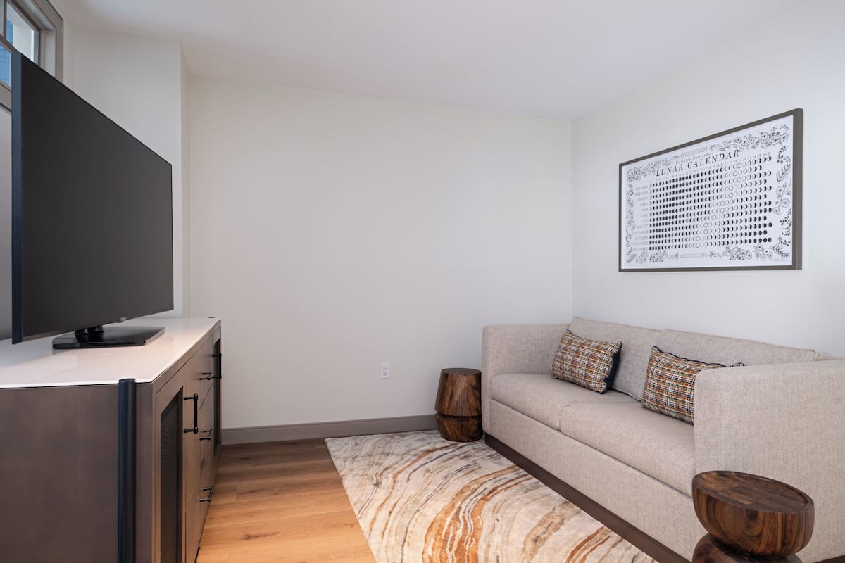 A modern living room with a flat-screen TV, a sofa, a patterned rug, and a wall-mounted calendar.