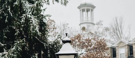 A snow-covered street lamp with a red bow, a church with a cross, and a building in the background.