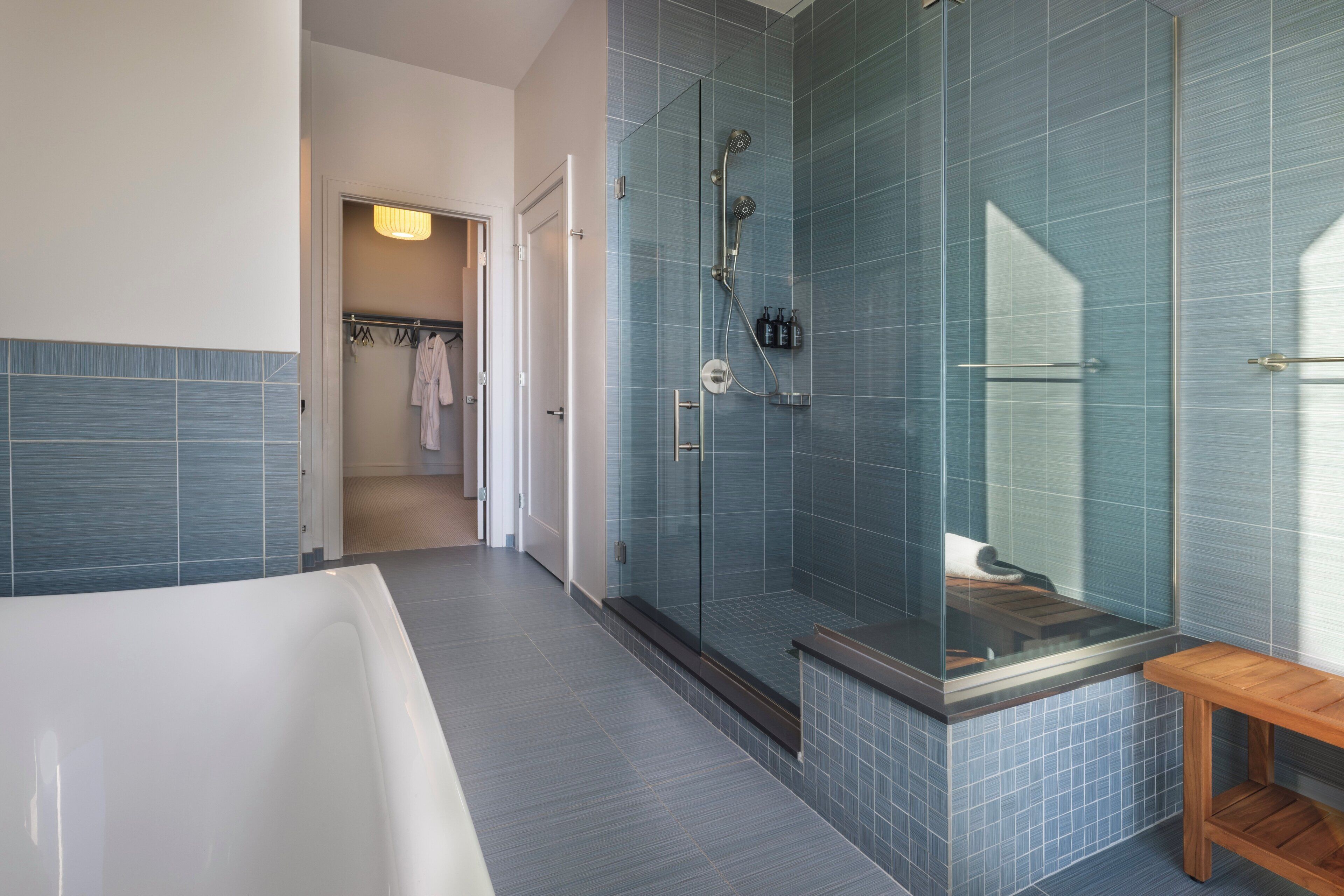 Un baño moderno con ducha de vidrio, bañera y banco de madera.