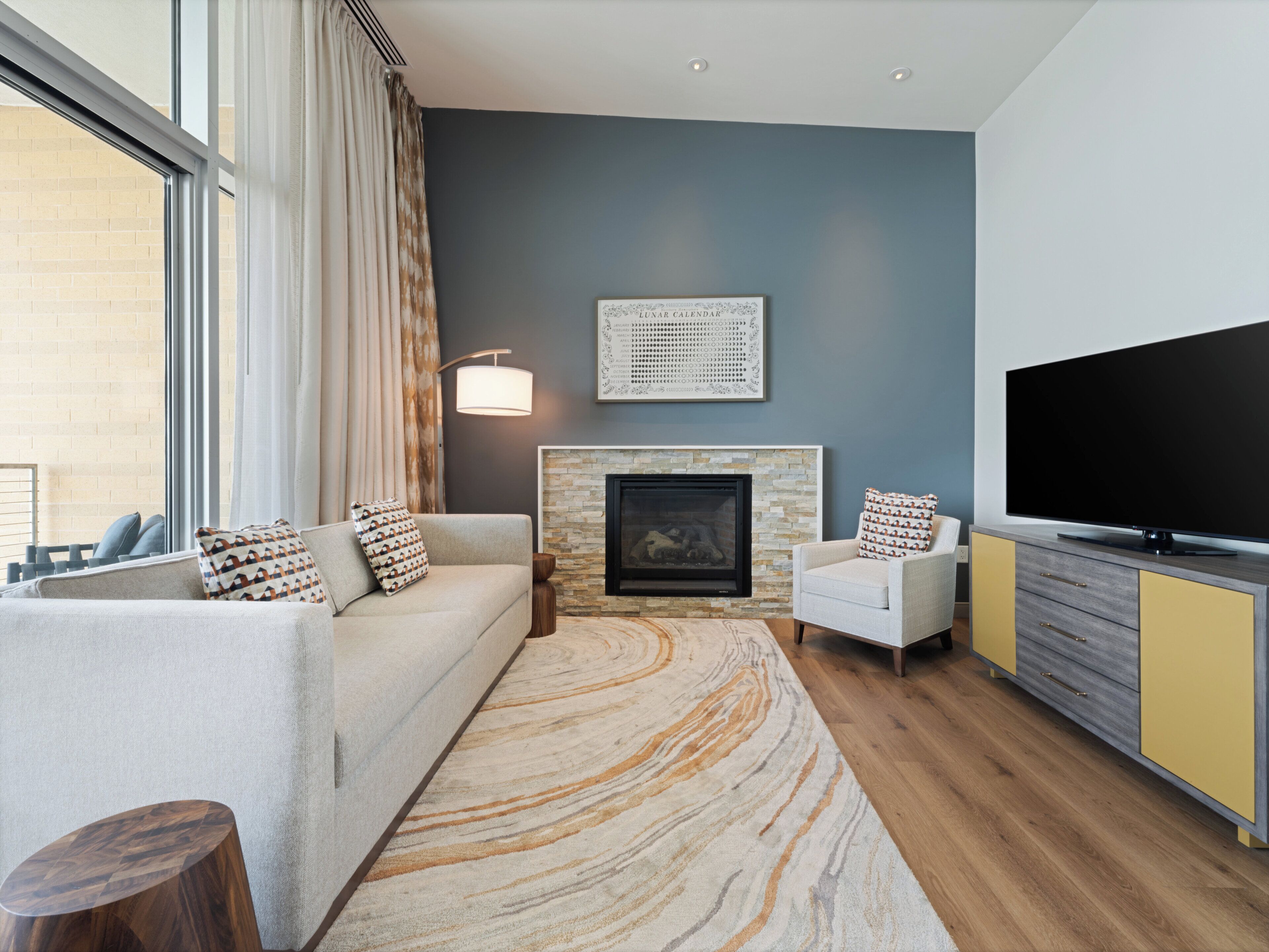 A modern living room with a sofa, armchair, fireplace, and a flat-screen TV.