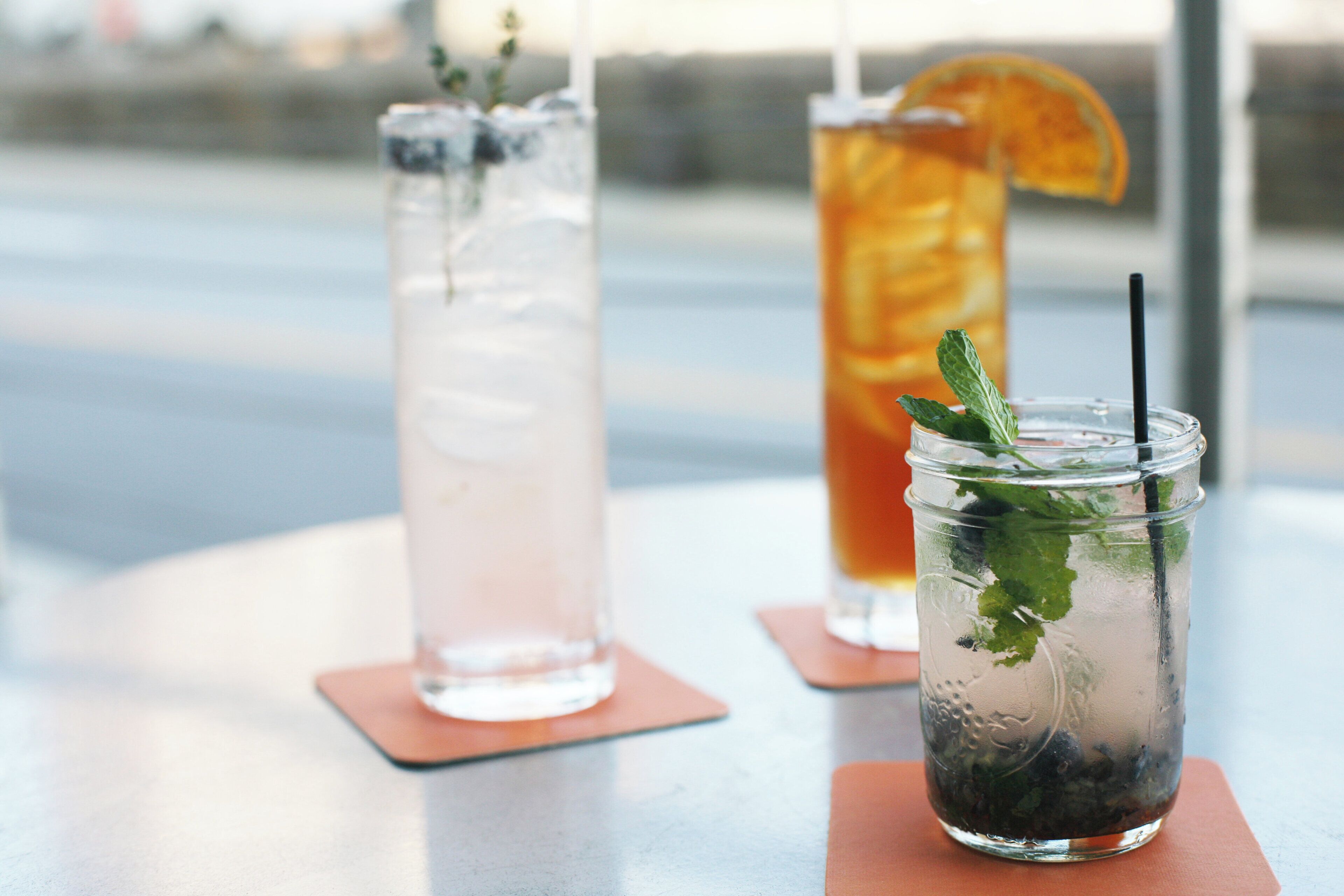 Two drinks on a table with a glass jar and a glass with a straw.