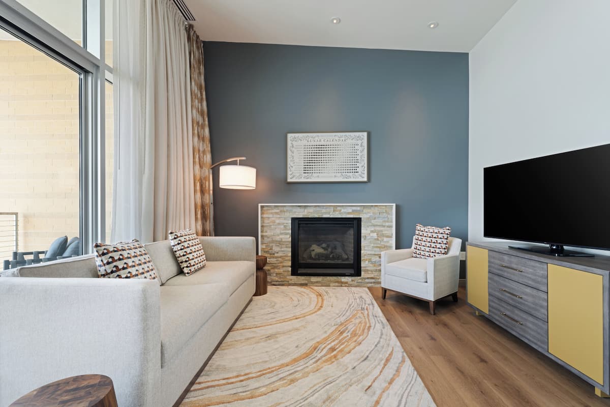 A modern living room with a sofa, armchair, fireplace, and a flat-screen TV.