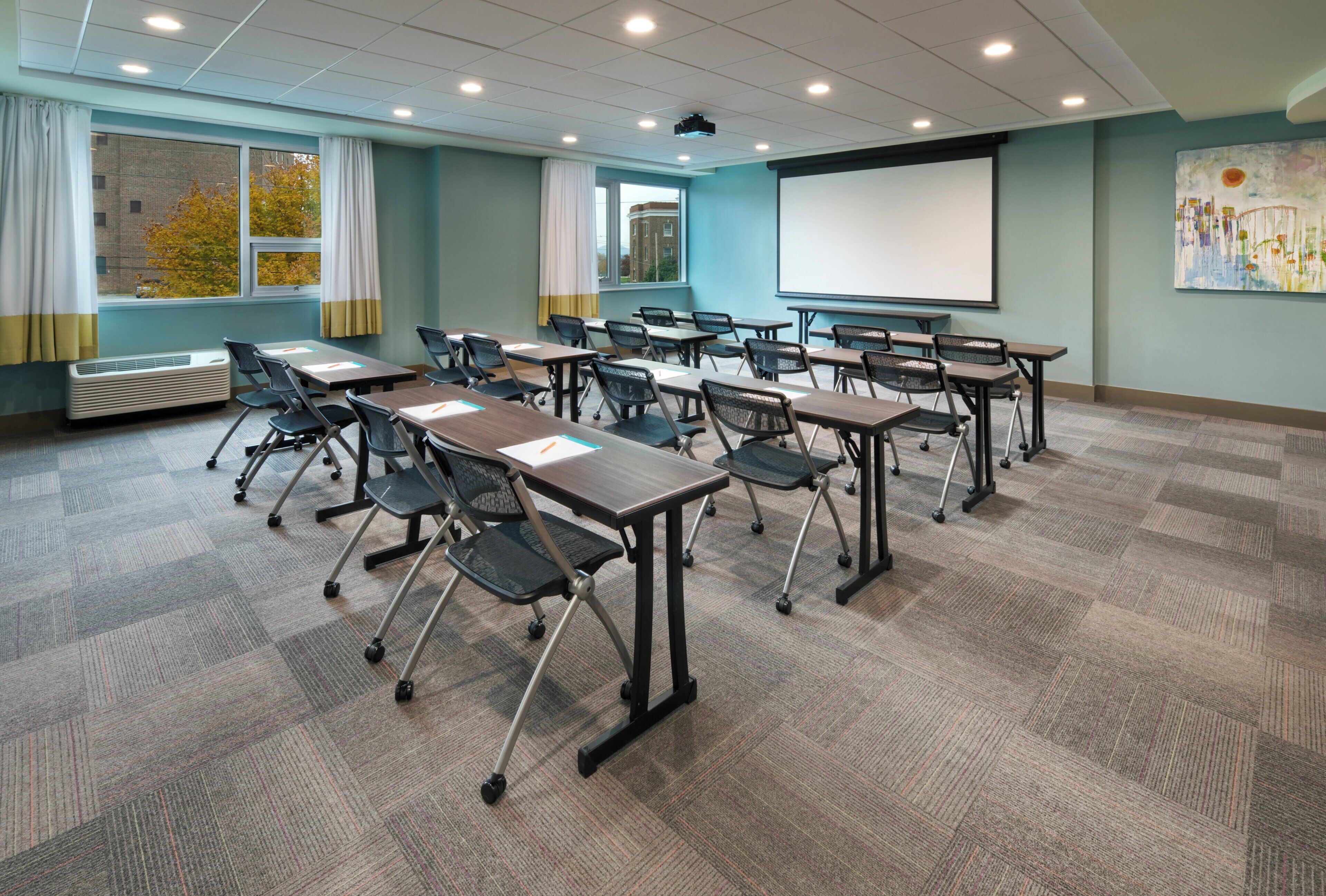 A conference room with tables, chairs, a projector screen, and a large window with curtains.