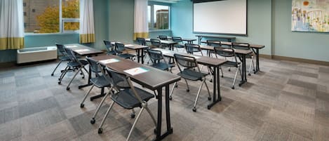 A conference room with tables, chairs, a projector screen, and a large window with curtains.