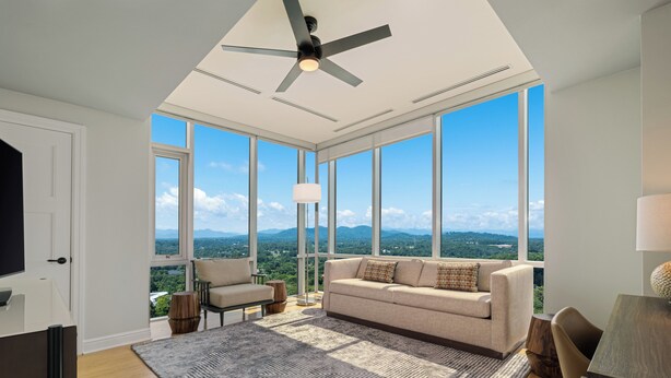 Uma sala de estar ampla com uma grande janela, um ventilador de teto e vista para as montanhas.
