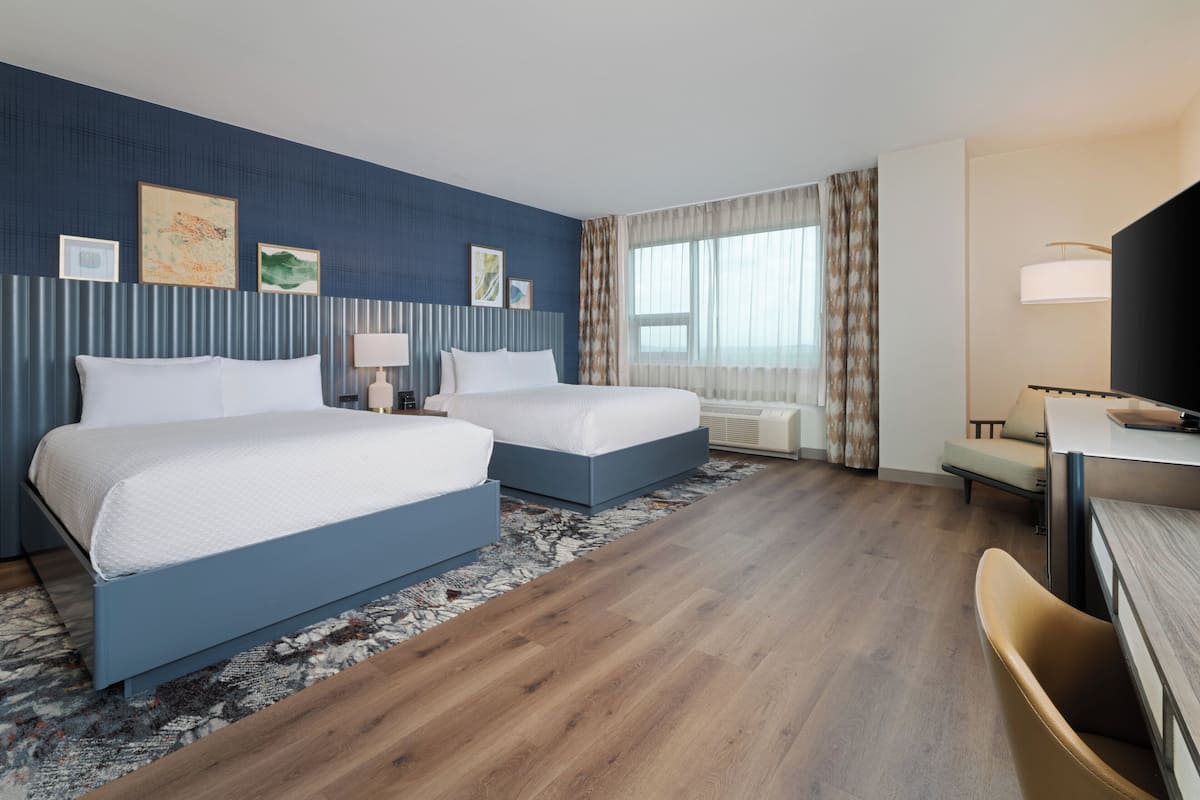 A hotel room with two beds, a desk, a TV, and a window with curtains.