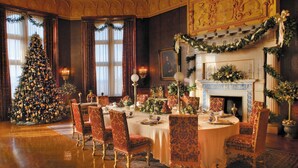 Uma sala de jantar formal com uma grande árvore de Natal, cadeiras ornamentadas e uma lareira.