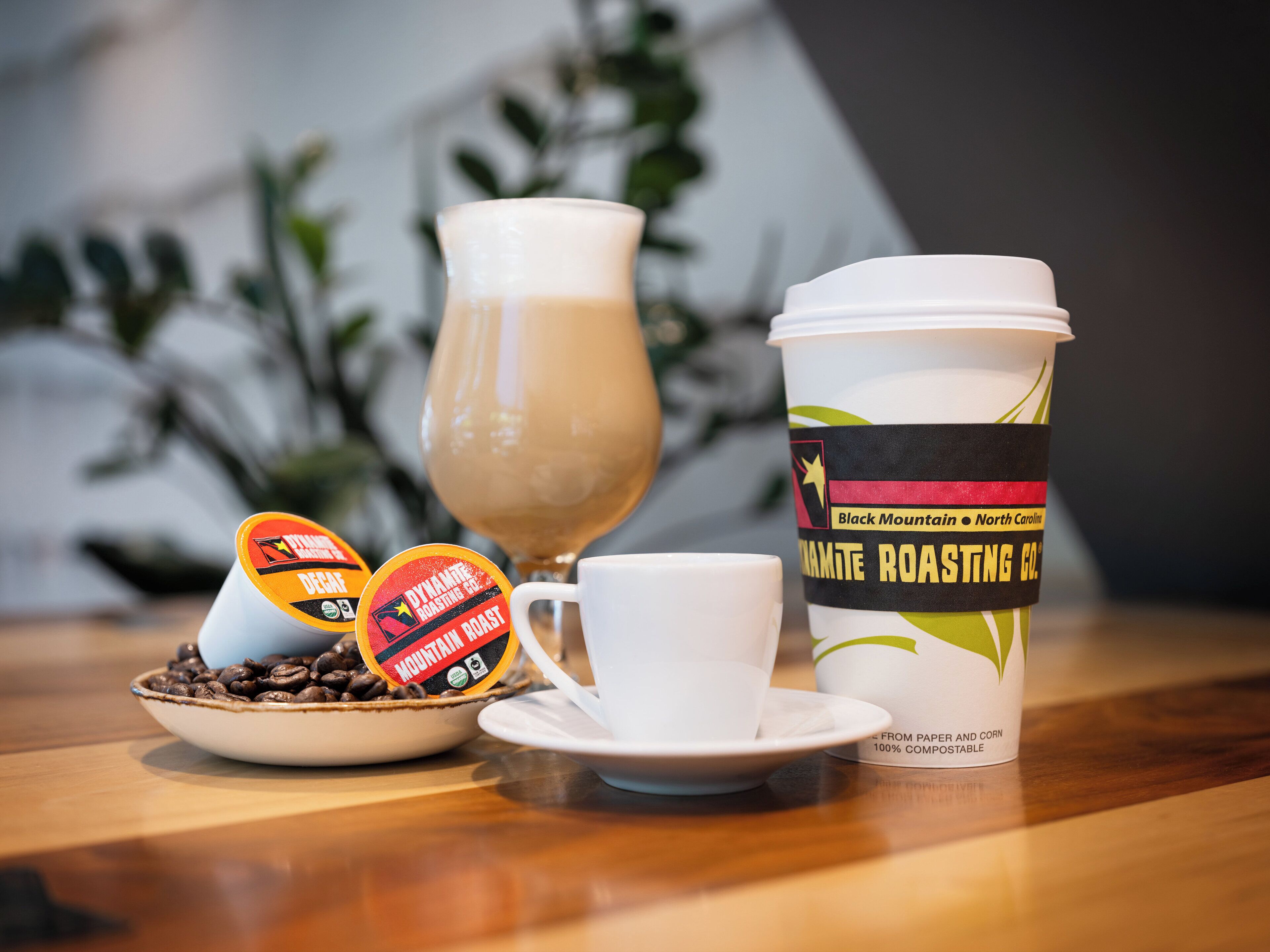 A coffee cup with a label, a glass of coffee, and two coffee pods on a table.