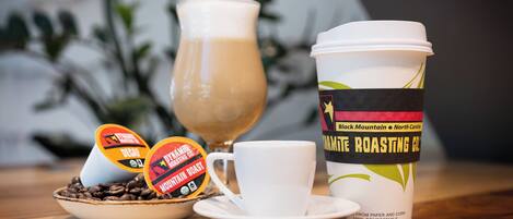 A coffee cup with a label, a glass of coffee, and two coffee pods on a table.