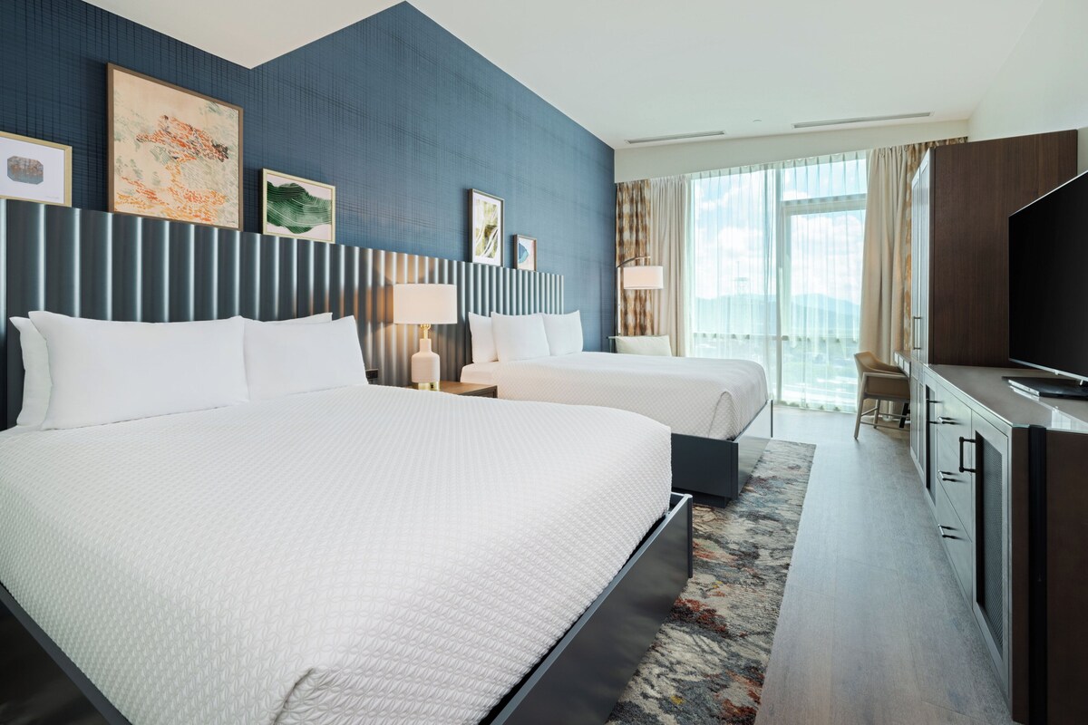 A hotel room with a large bed, a desk with a TV, and a window with curtains.