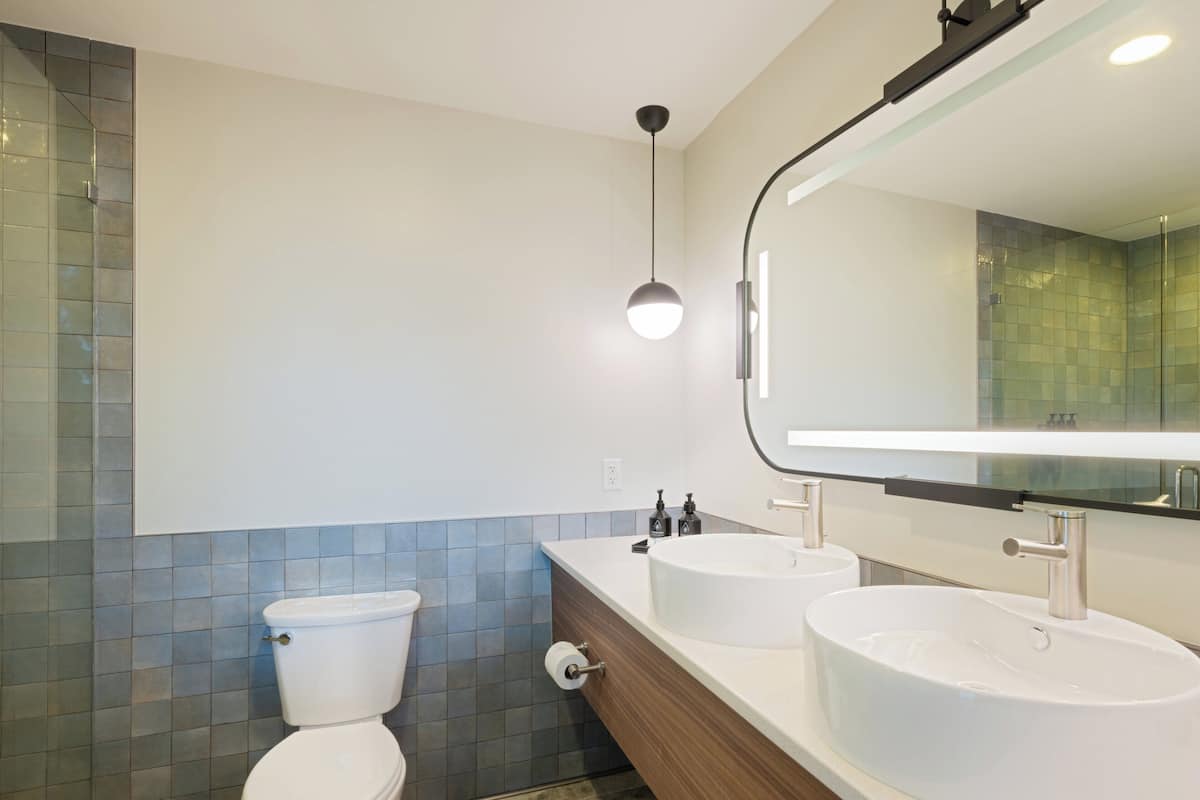A modern bathroom with a toilet, two sinks, and a mirror.