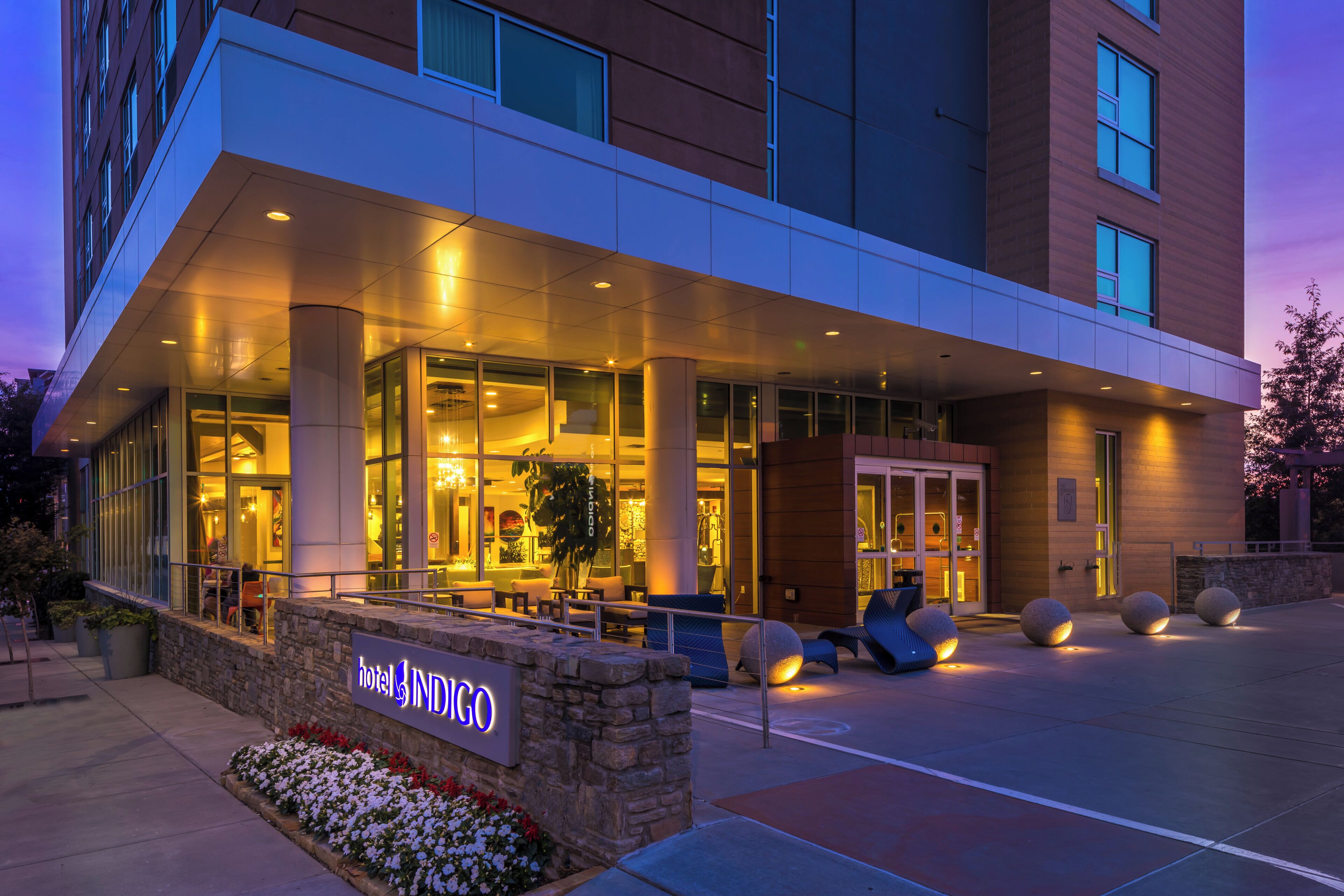 A hotel entrance with a modern design, including a glass facade, outdoor seating area, and a sign indicating the hotel name.
