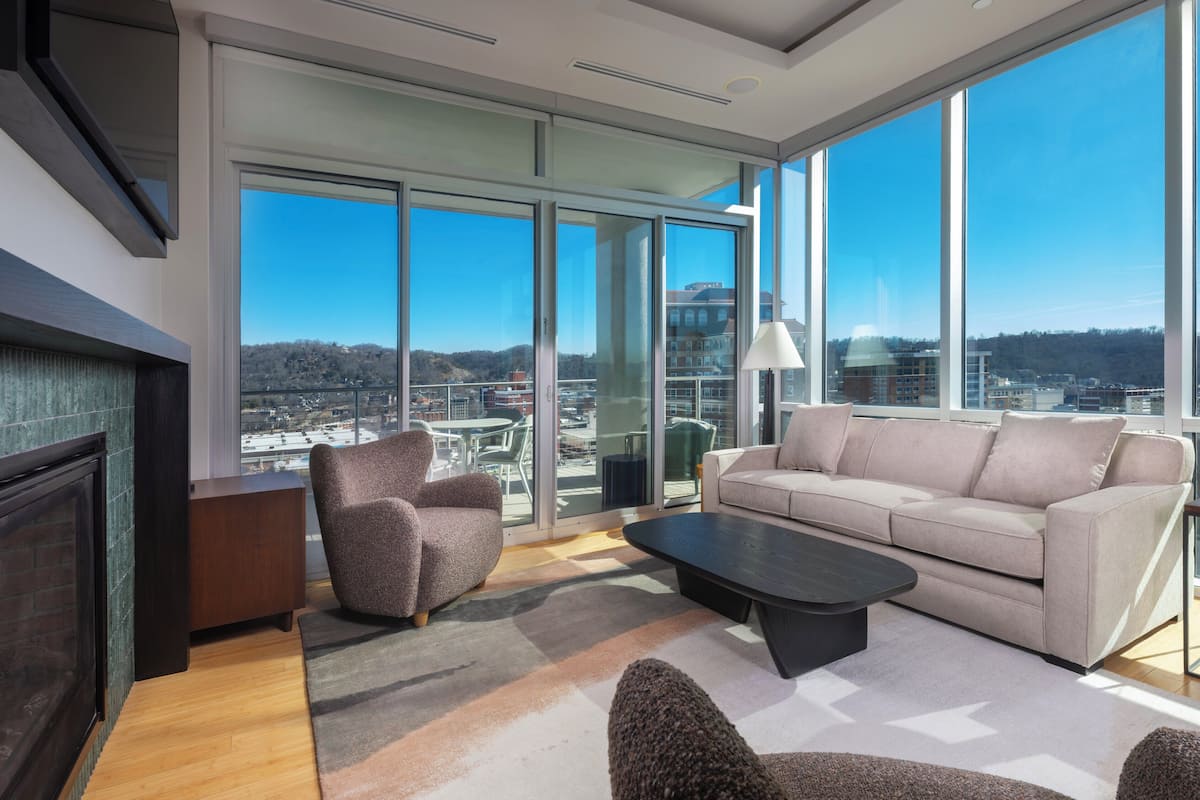 A modern living room with a large window, a fireplace, a sofa, and a coffee table.