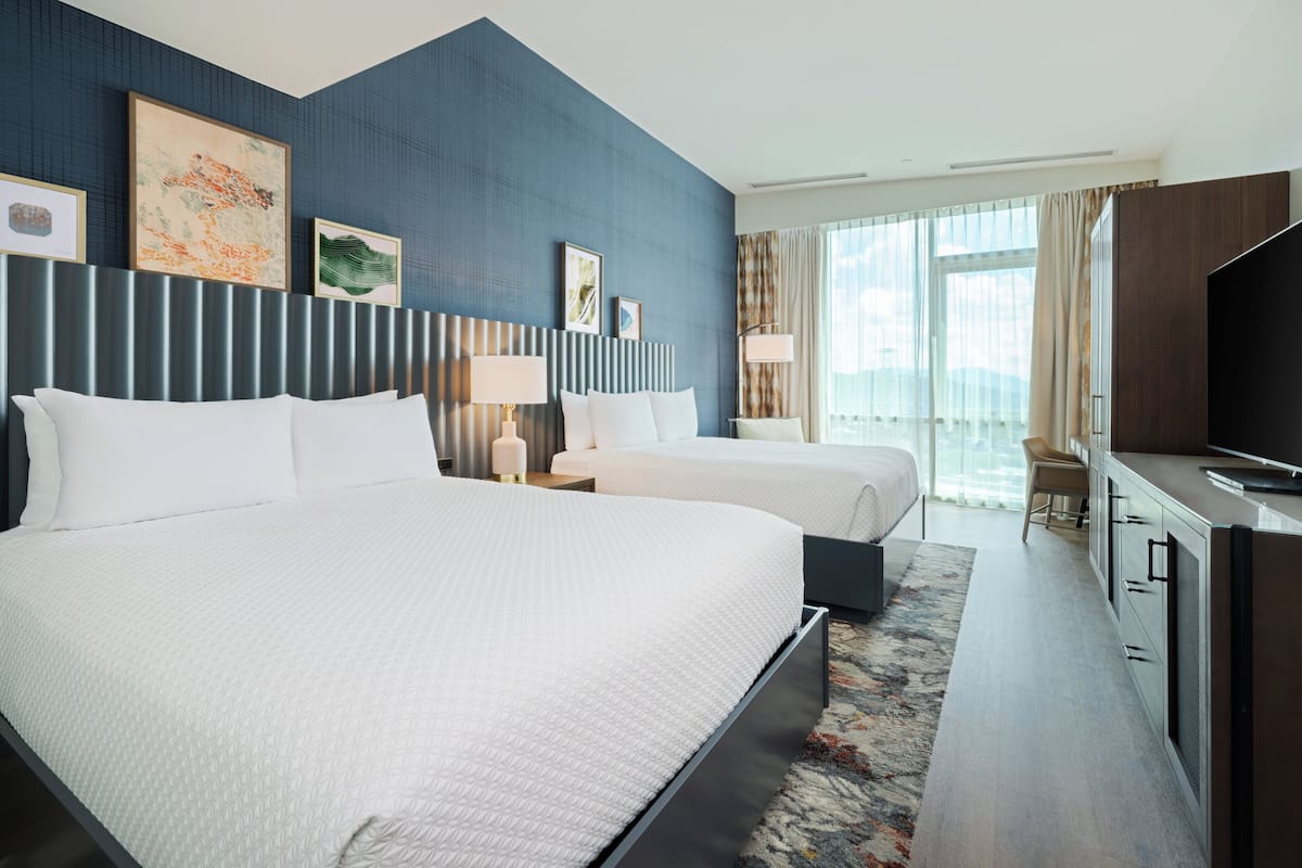 A hotel room with a large bed, a desk with a TV, and a window with curtains.