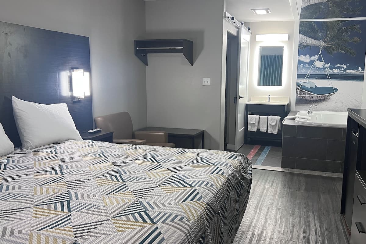 A hotel room with a bed, a desk, a chair, a bathroom with a sink and mirror, and a view of the ocean through the window.