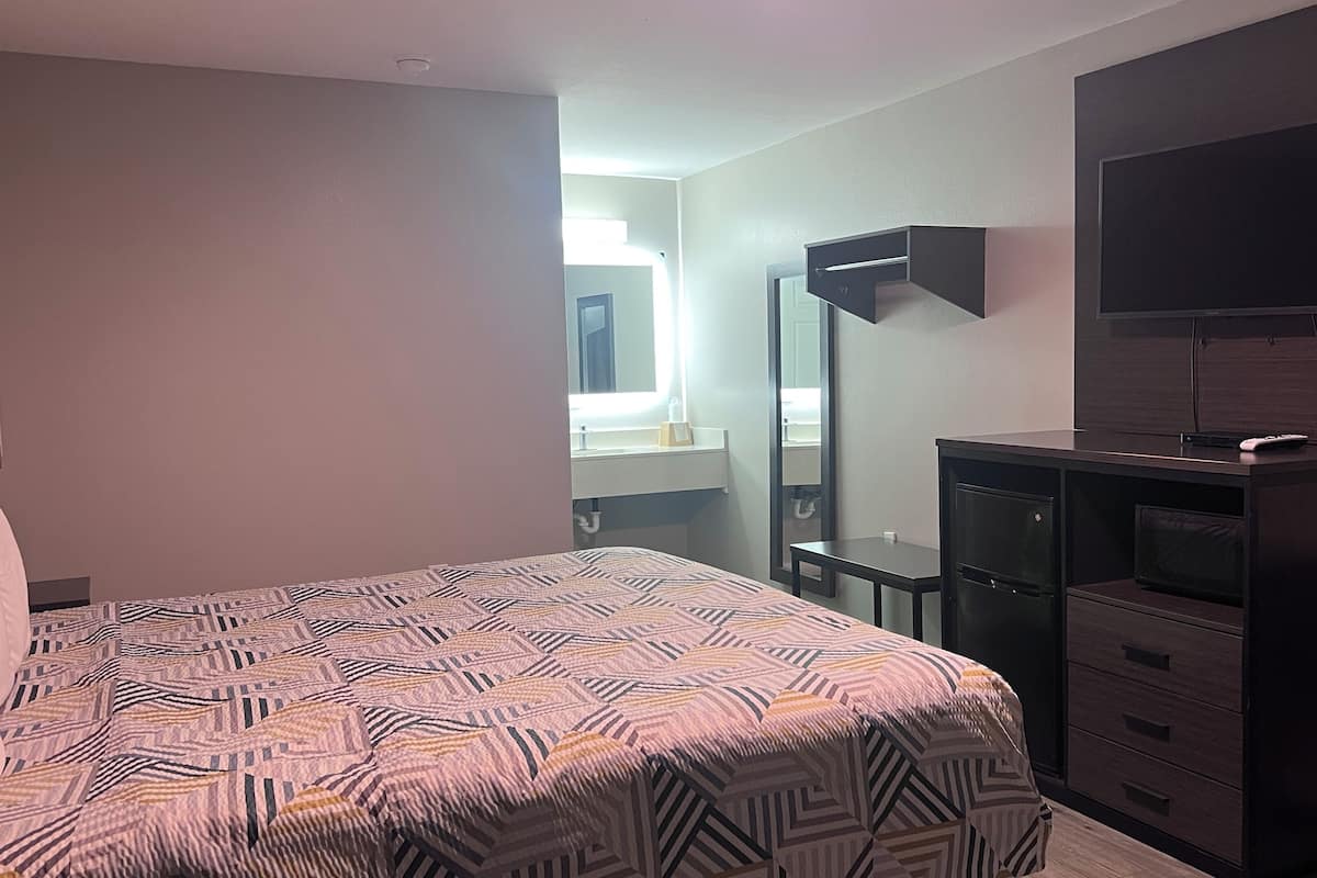 A hotel room with a bed, a dresser, a TV, and a bathroom visible in the background.