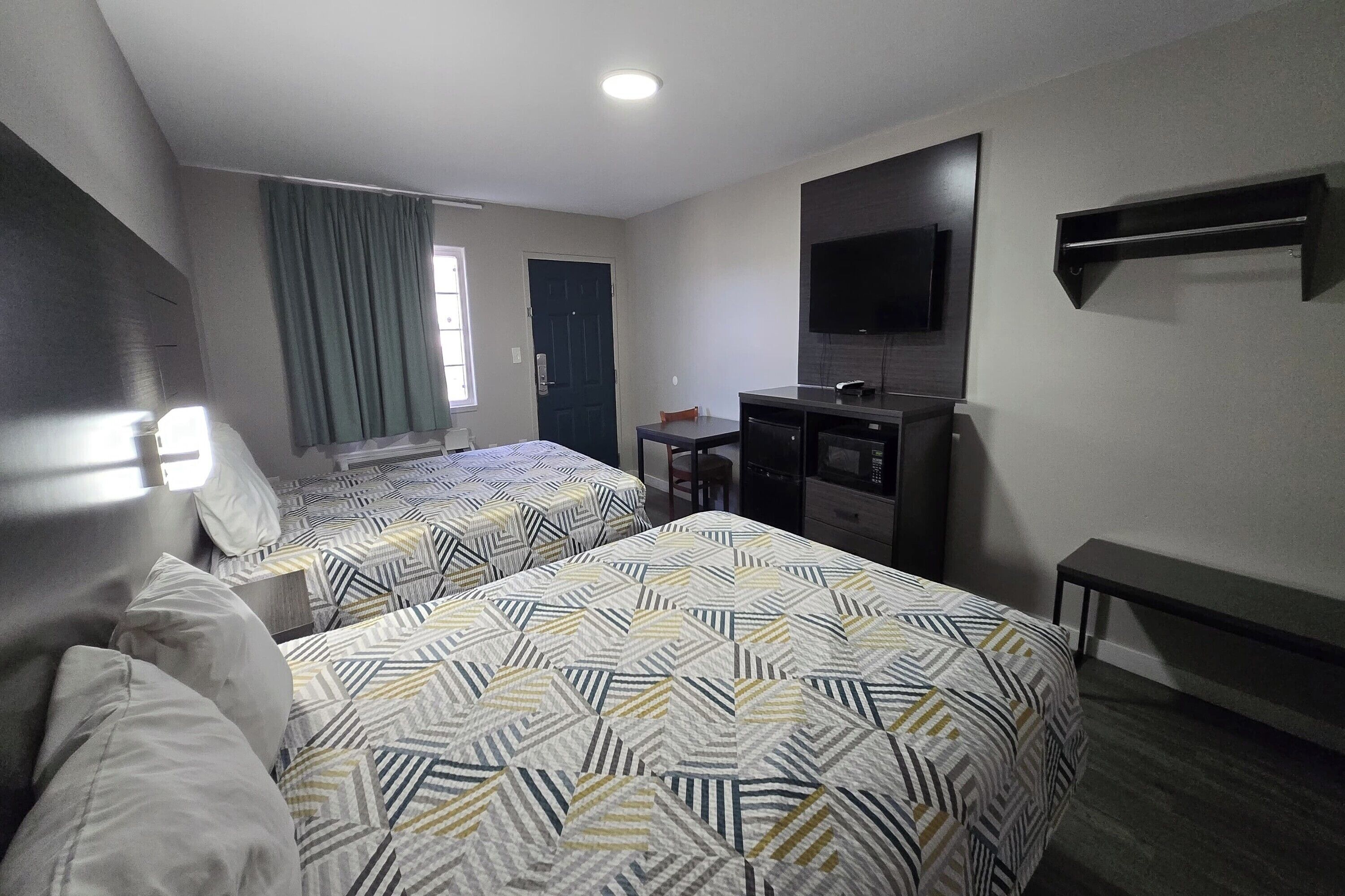 A hotel room with two beds, a desk, a television, and a window with curtains.