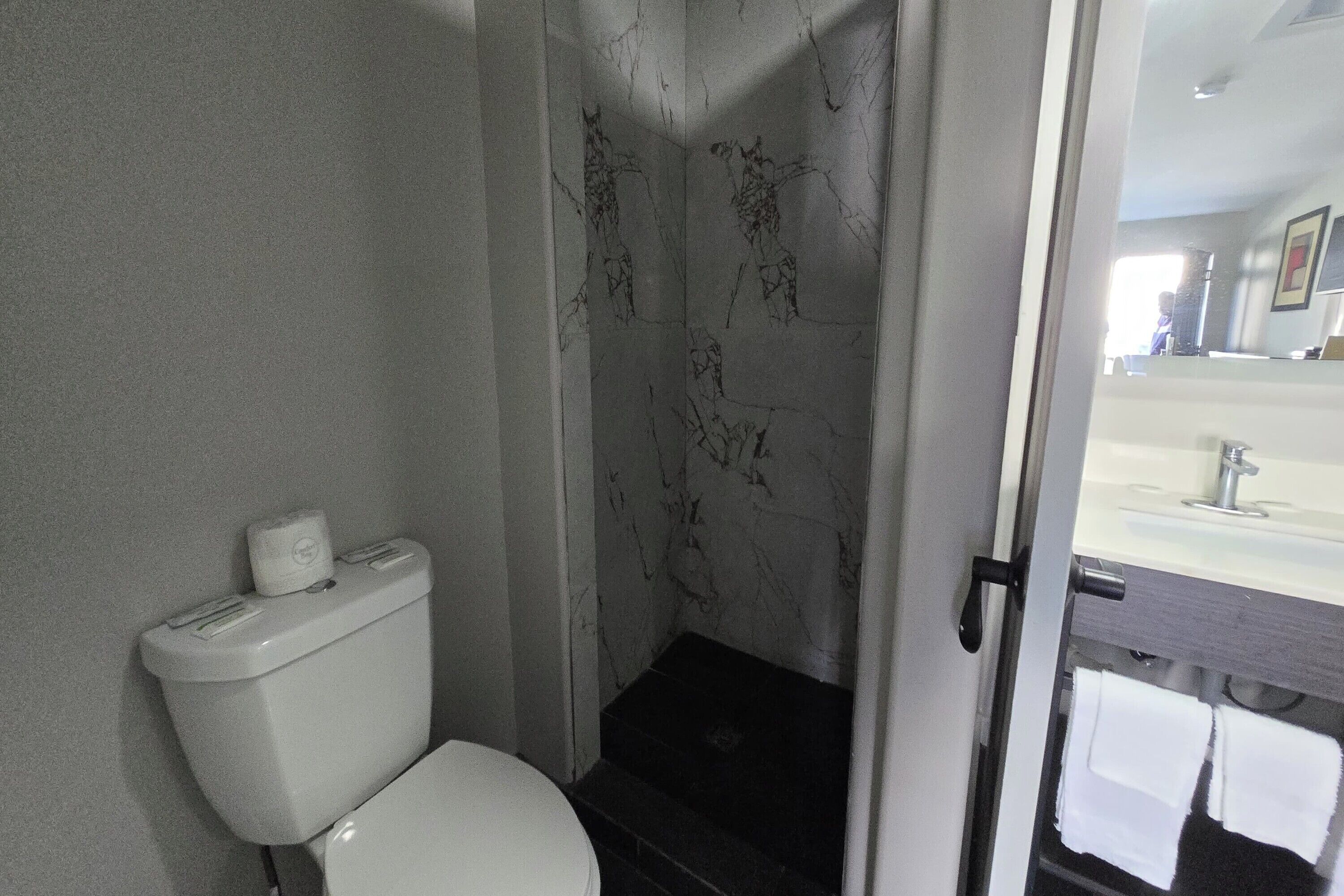 Un baño con inodoro, ducha con pared de mármol y zona de lavamanos visible.