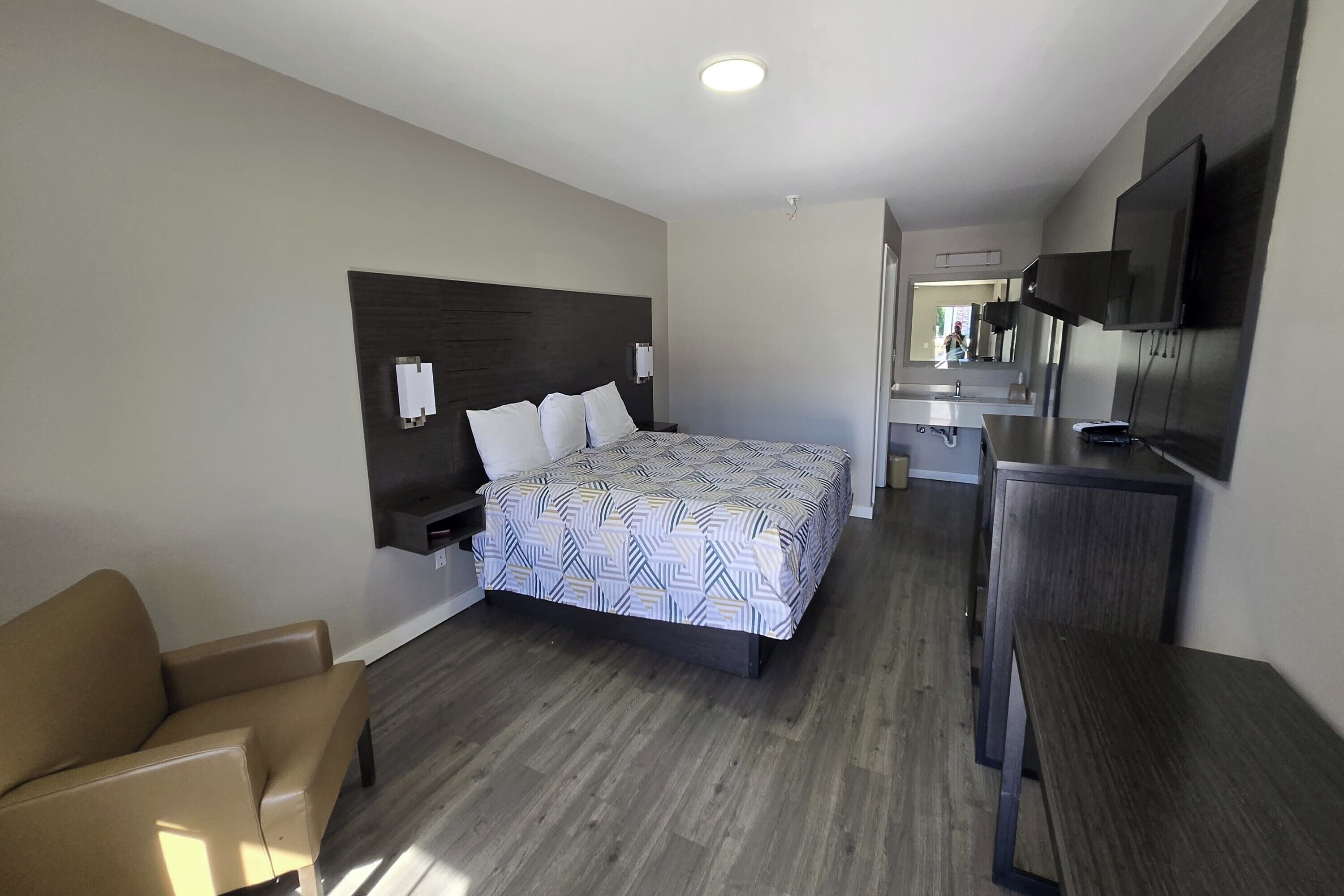 A modern hotel room with a large bed, a sofa, a TV, and a small desk area.