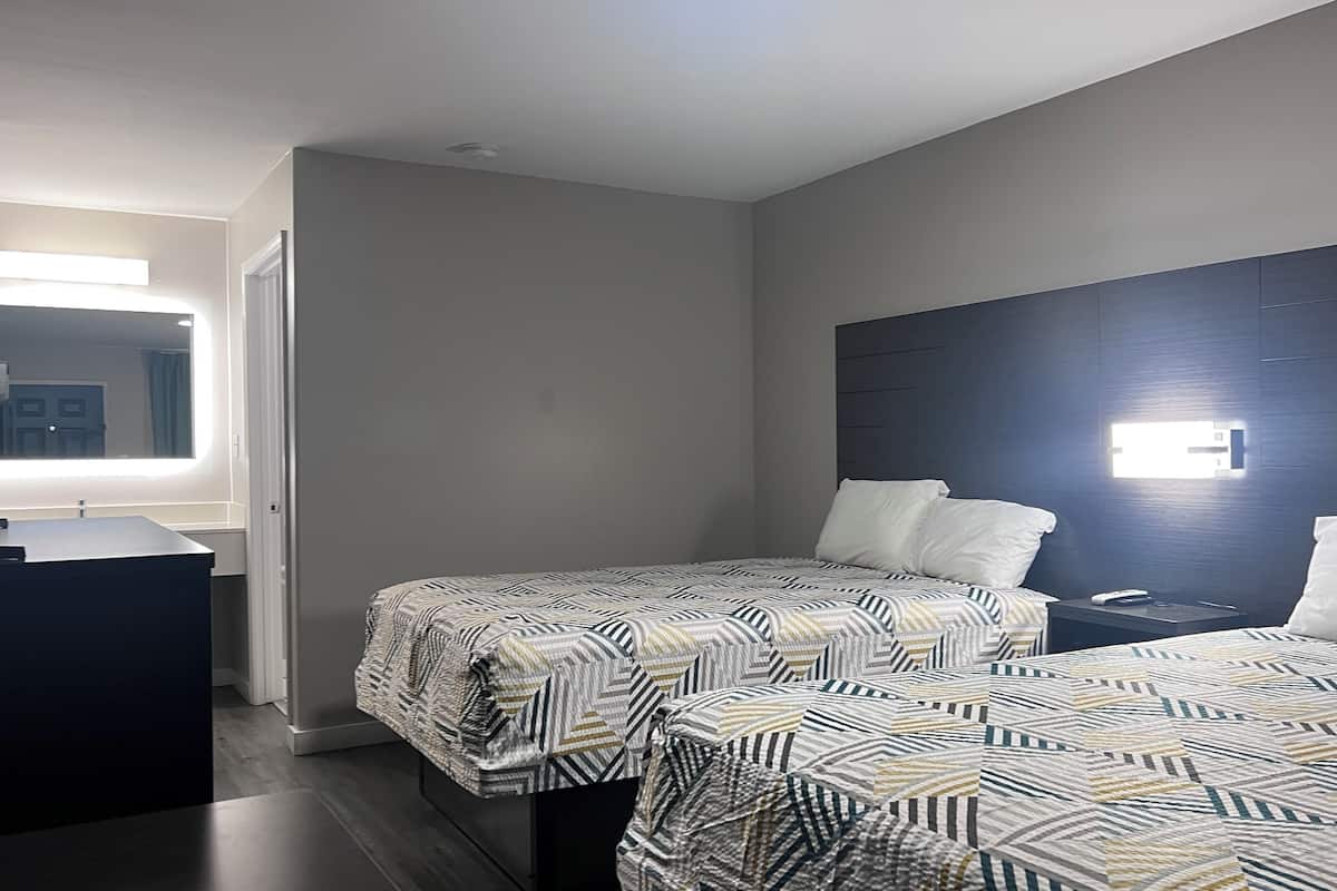 A hotel room with two beds, a desk, and a mirror.