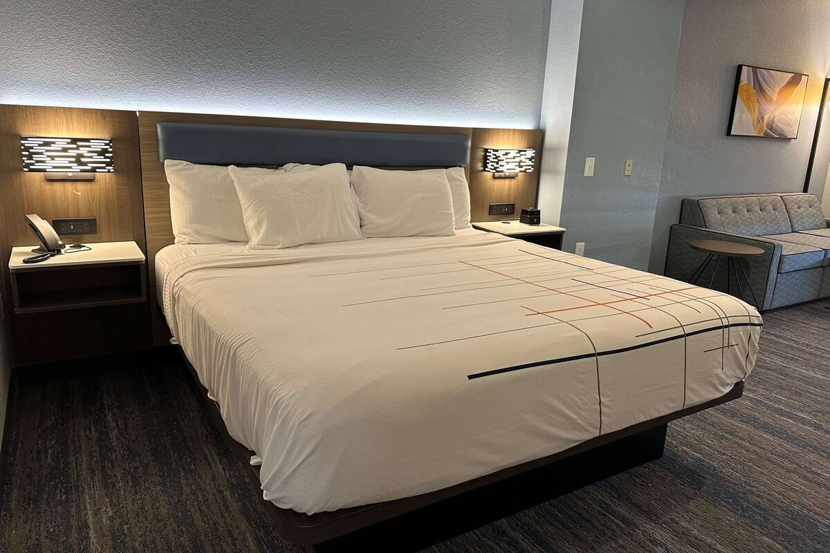 Ein Hotelzimmer mit einem großen Bett, zwei Nachttischen, einem Sessel und einem Wandbild.