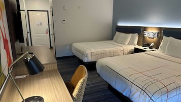 A hotel room with two beds, a desk with a lamp, a chair, and a nightstand with a phone.