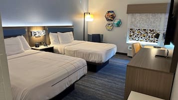 Habitación de hotel con dos camas, un escritorio, una silla, un televisor y un ventanal con cortinas estampadas.