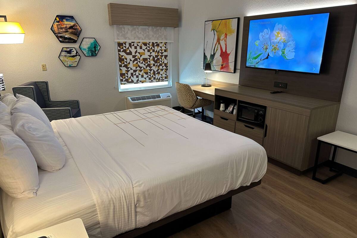 Ein modernes Hotelzimmer mit einem großen Bett, einem Schreibtisch mit Stuhl, einem Flachbildfernseher und Bildern an den Wänden.