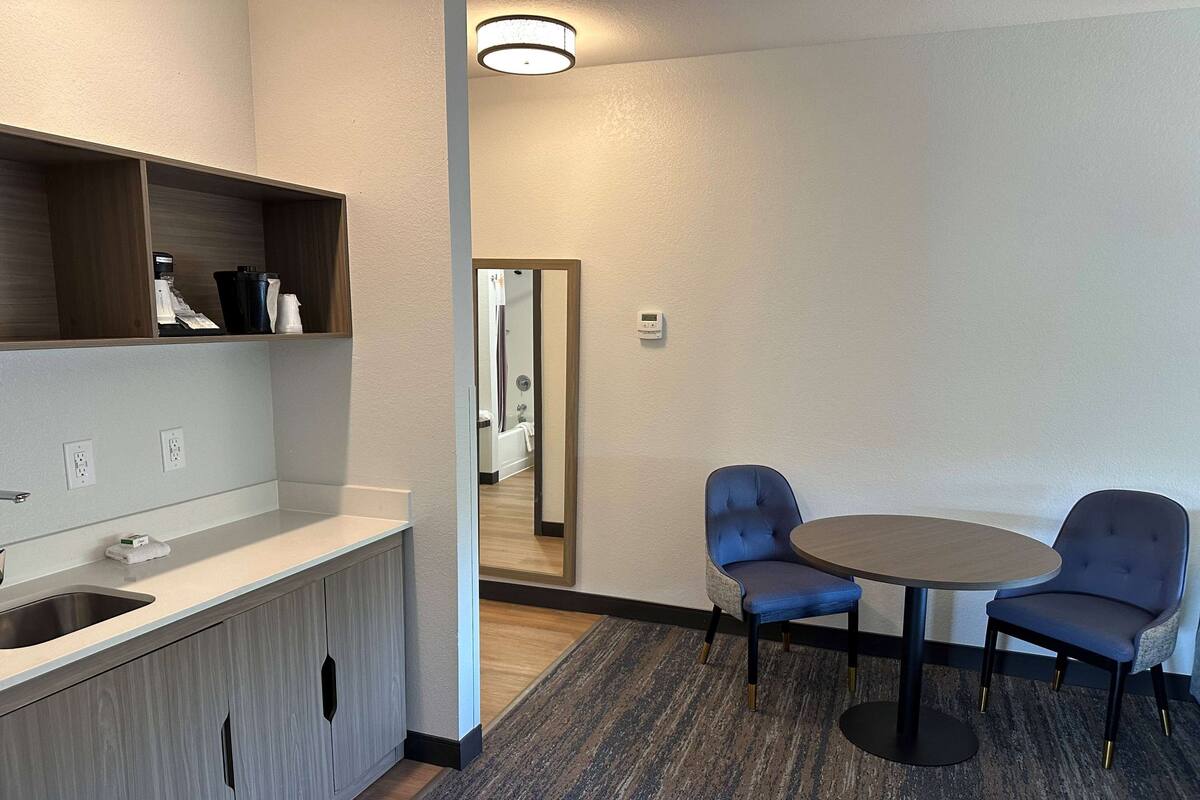 Ein modernes Hotelzimmer mit einem Holznähtisch, einem Waschbecken, einem Spiegel und einem runden Tisch mit zwei Stühlen.