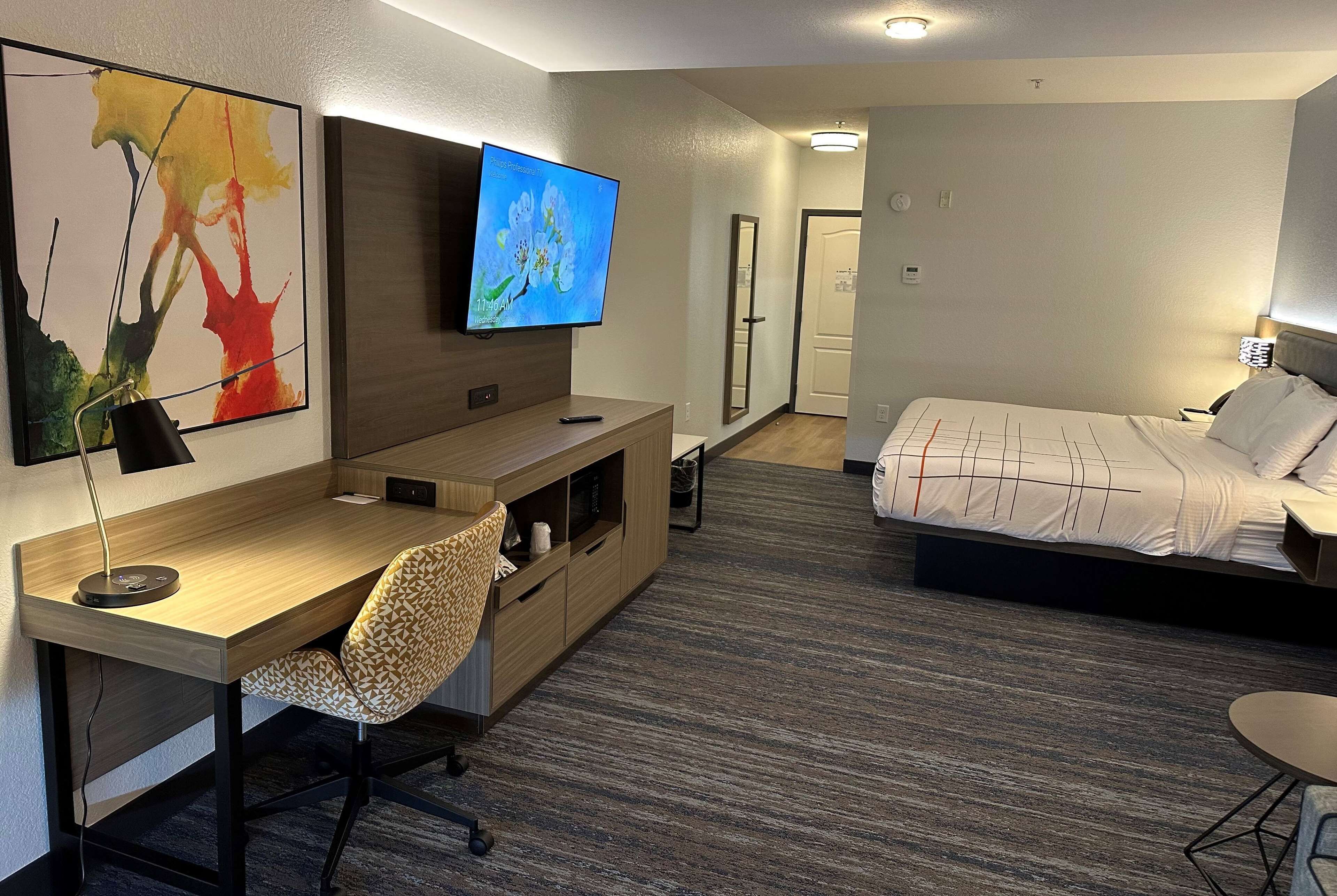 Ein Hotelzimmer mit Holzschreibtisch, Stuhl, Bett, Fernseher und Spiegel.
