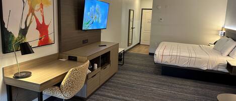 Una habitación de hotel con un escritorio de madera, una silla, una cama, un televisor y un espejo.