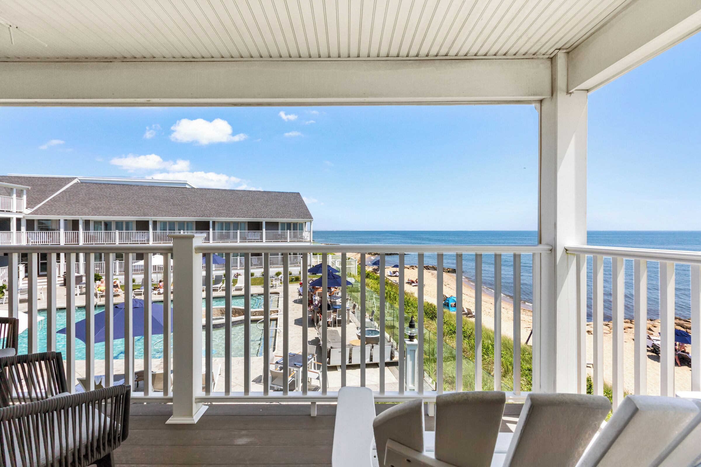 Ein Balkon mit Blick auf einen Pool und Strand, inklusive Liegestühle und Sonnenschirme.