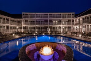 A swimming pool with a fire pit in the center, surrounded by lounge chairs and a multi-story building with balconies. - Pelham House Resort (Dennis Port)