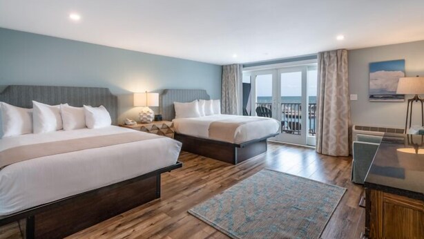 A hotel room with two beds, a desk, and a view of the sea.