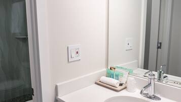 Un baño con lavamanos blanco, un espejo y zona de ducha.