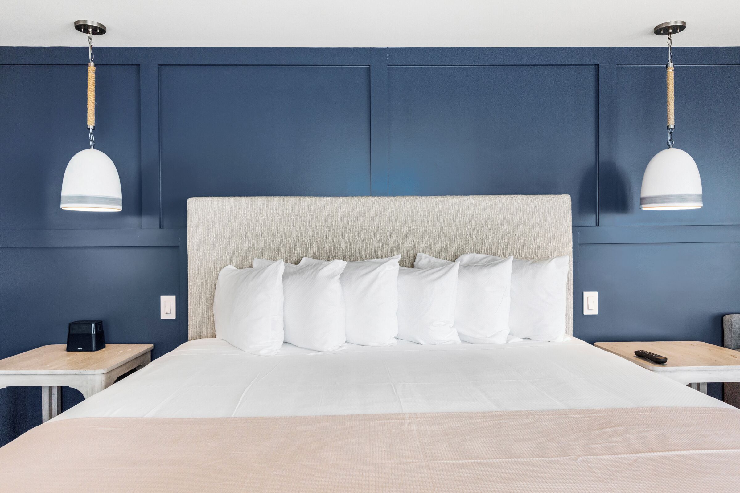 A hotel room with a large bed, two bedside tables, a nightstand, and two pendant lights.